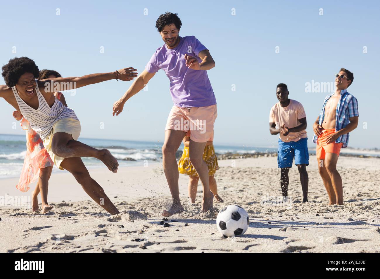 Amici eterogenei si divertono a giocare a calcio sulla spiaggia Foto Stock