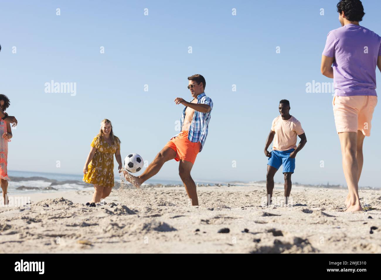 Un gruppo eterogeneo di amici, giovani adulti, si diverte a giocare a calcio in spiaggia Foto Stock