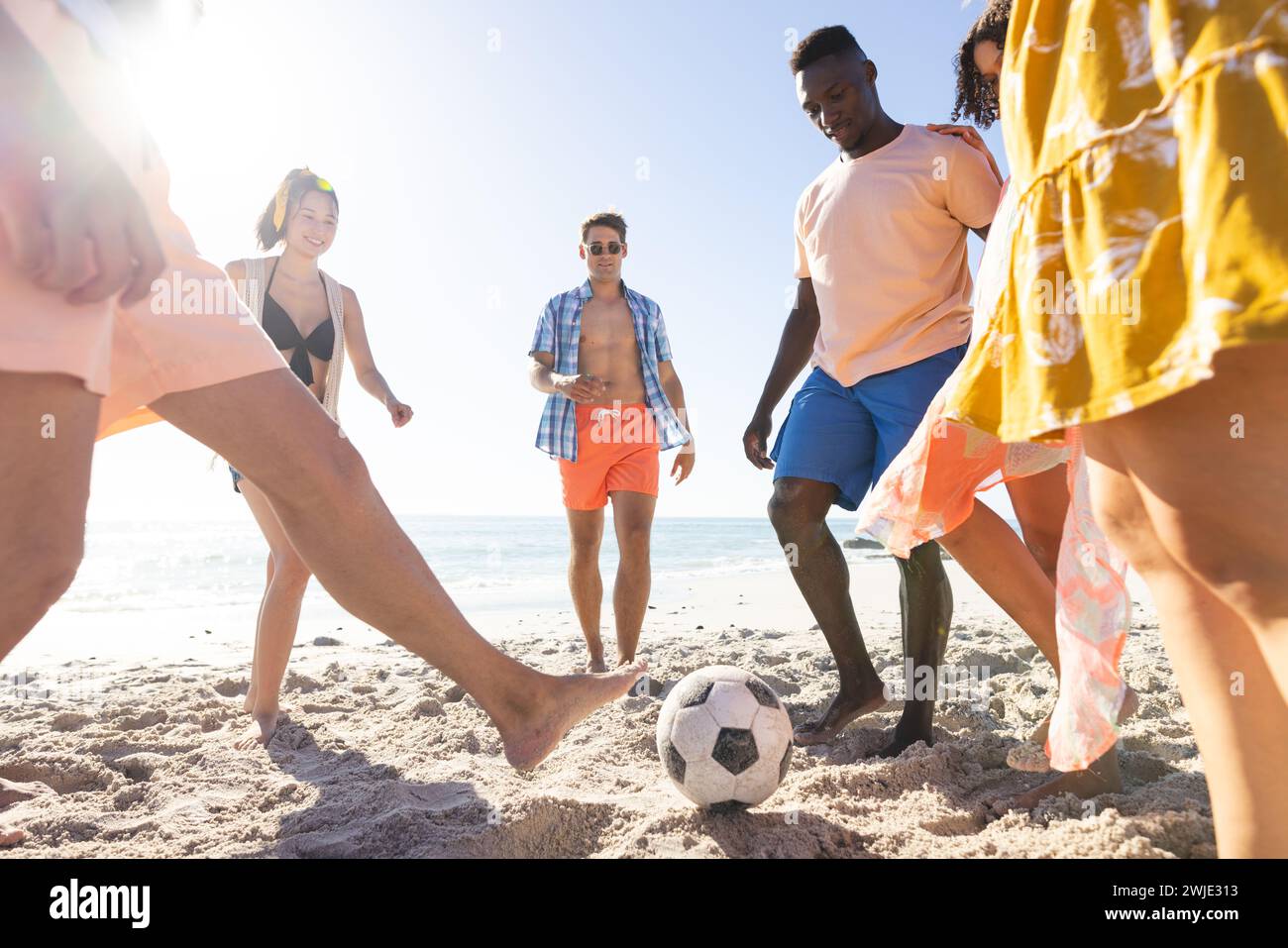 Amici diversi si divertono a giocare a calcio sulla spiaggia Foto Stock