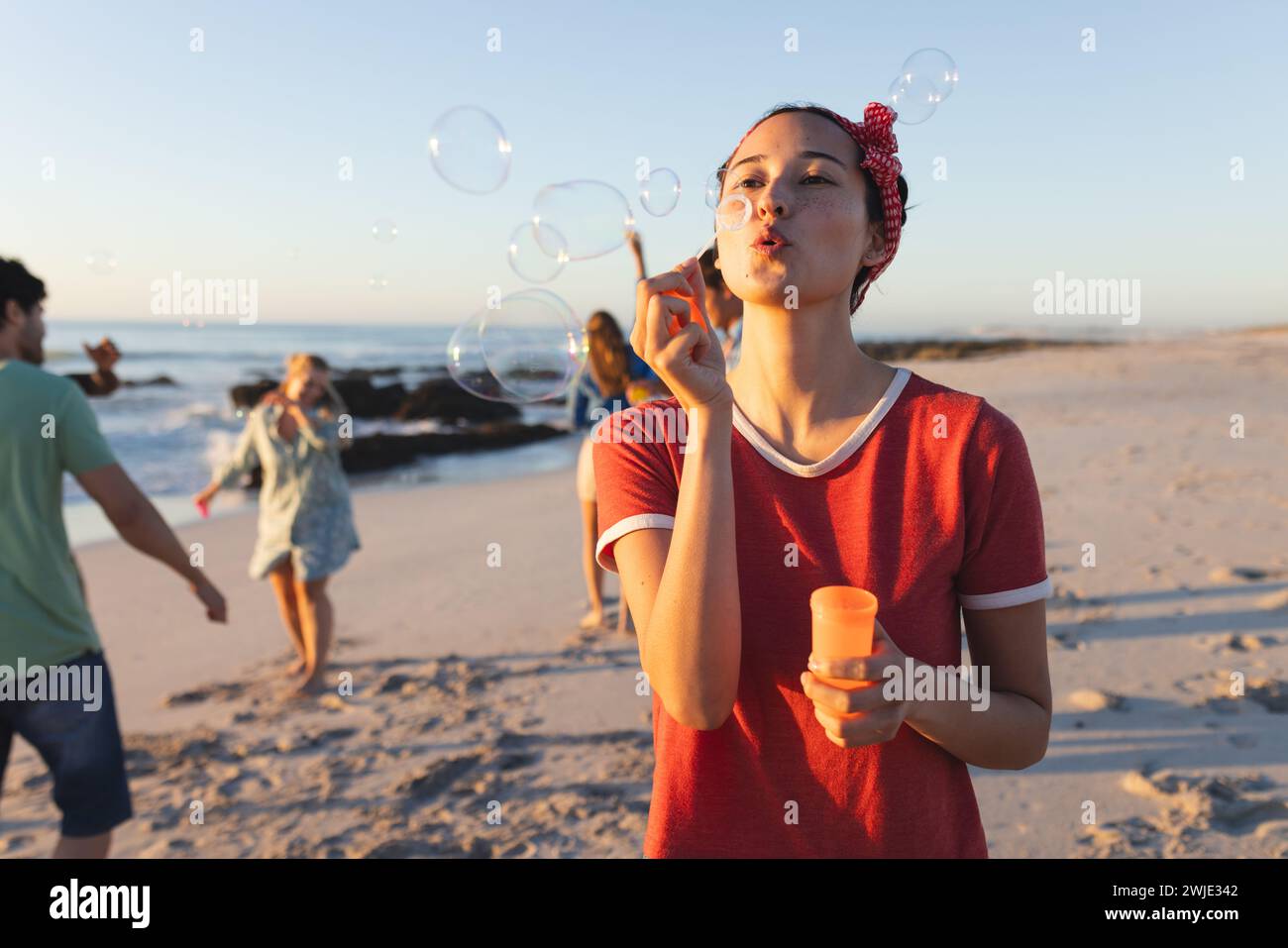 La giovane donna caucasica soffia bolle su una spiaggia al tramonto Foto Stock