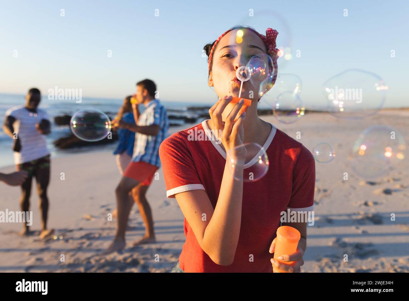 La giovane donna caucasica soffia bolle su una spiaggia soleggiata Foto Stock