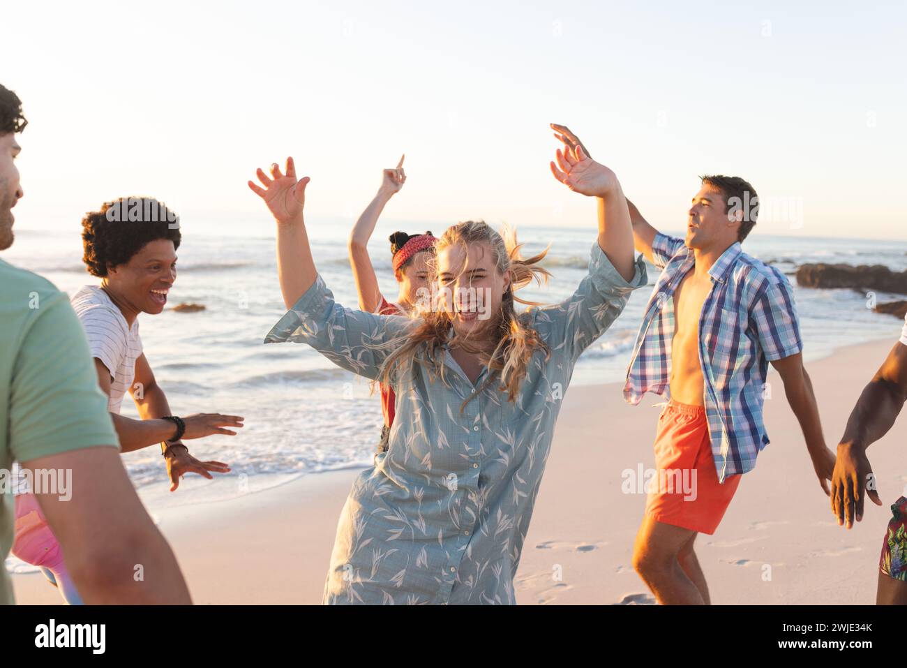 Gli amici si godono una vivace festa in spiaggia al tramonto Foto Stock