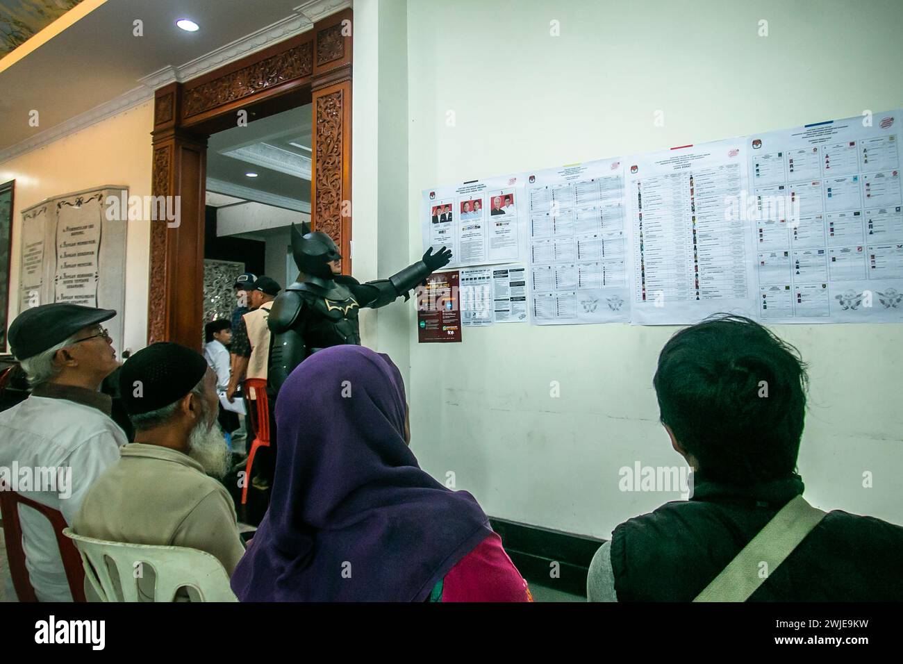 Un funzionario delle elezioni che indossa un costume di Batman lavora durante la presidenza indonesiana in un seggio elettorale a Bogor, Indonesia, il 14 febbraio 2024 Foto Stock