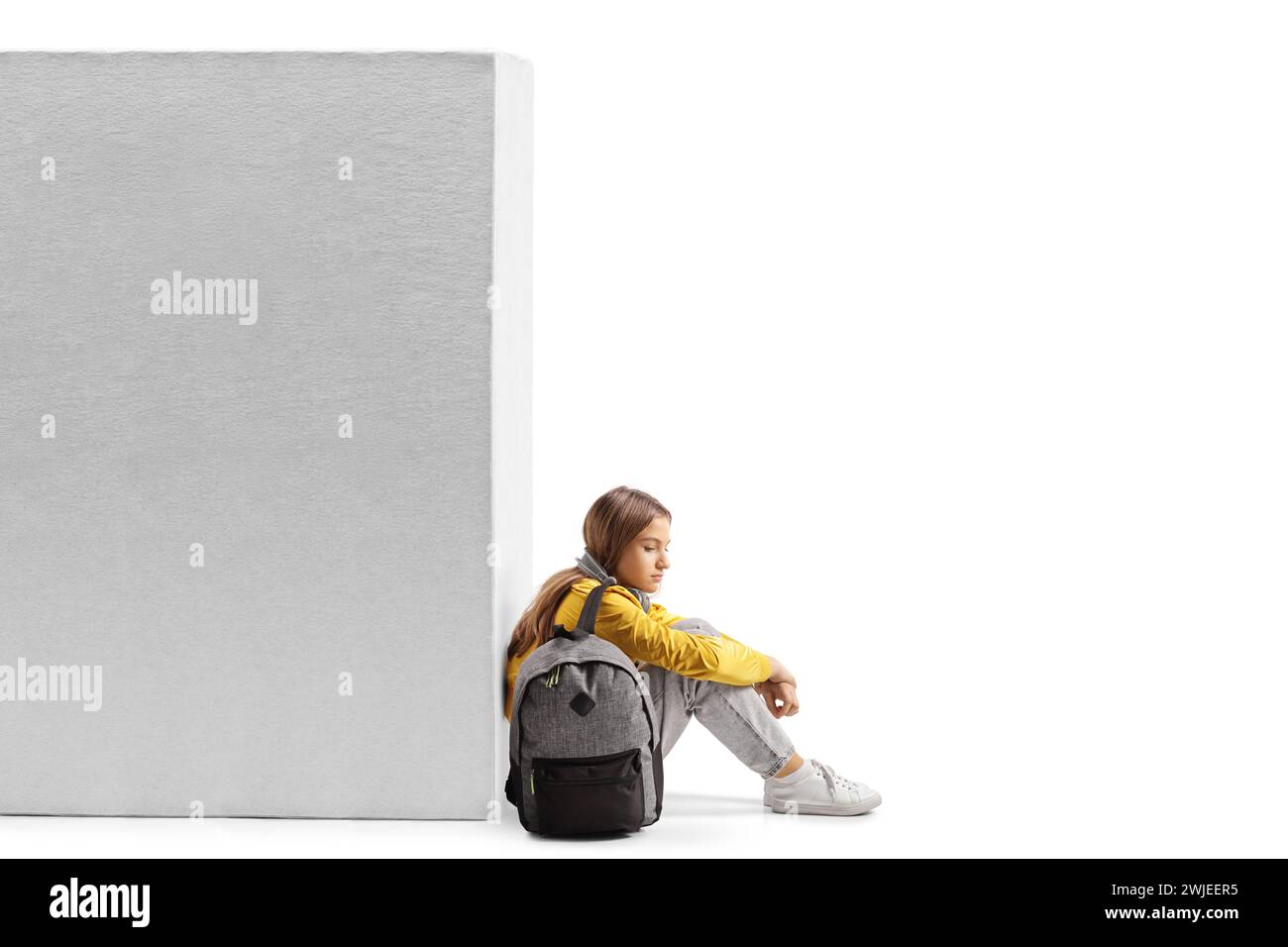 Triste adolescente seduta accanto a un muro isolata su sfondo bianco Foto Stock
