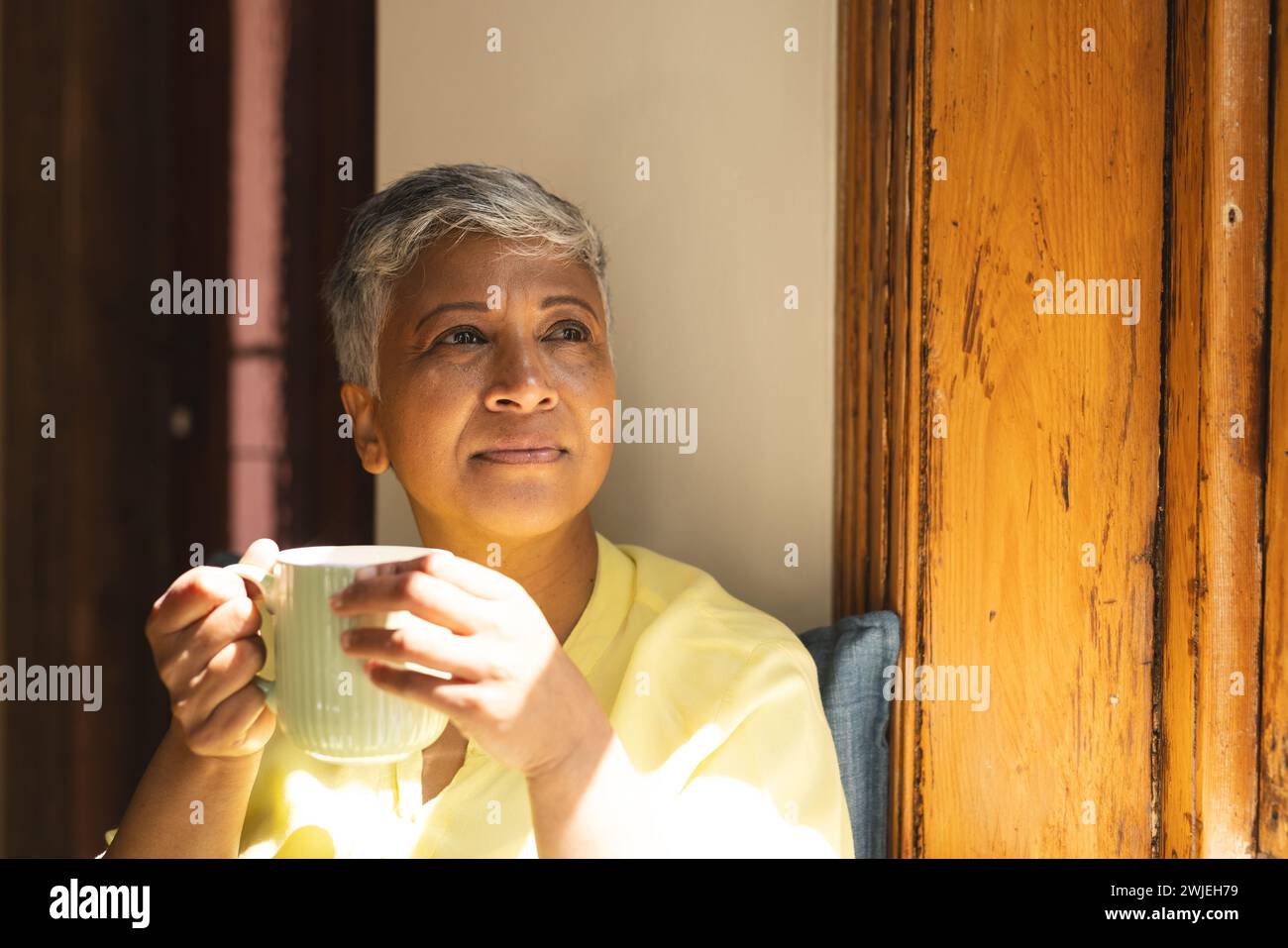 Una donna birazziale matura e premurosa si gode una tazza di tè a casa Foto Stock