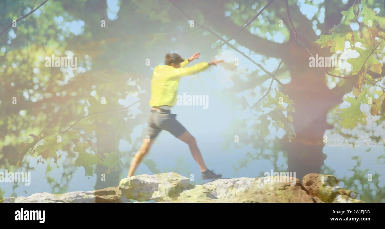 L'uomo salta sulle rocce di montagna, alza le mani in trionfo, gli alberi in primo piano Foto Stock