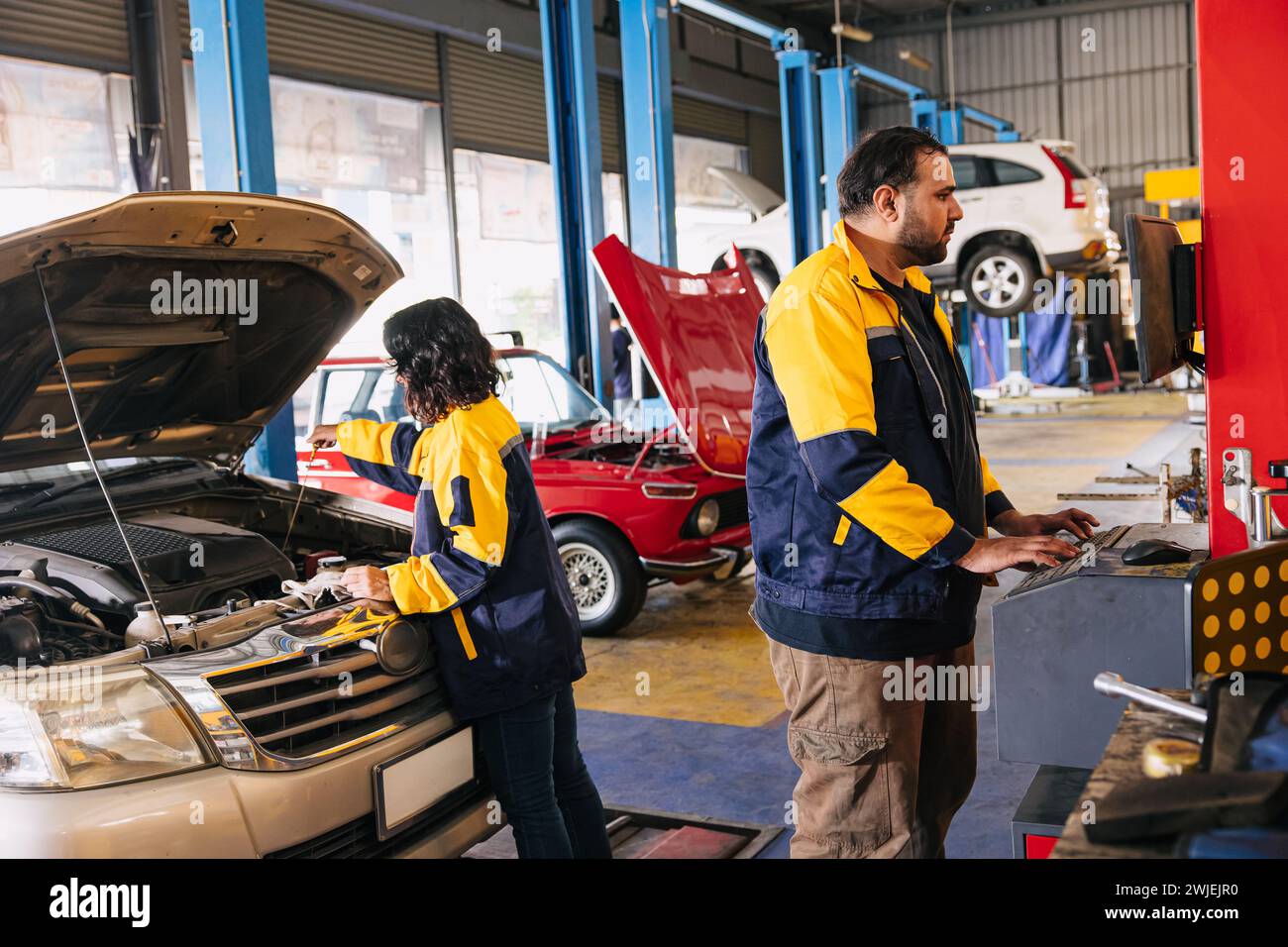 Lavoro di squadra del meccanico del garage per controllare il livello dell'olio motore con l'avambraccio nel lavoro di squadra del personale del centro di assistenza auto Foto Stock