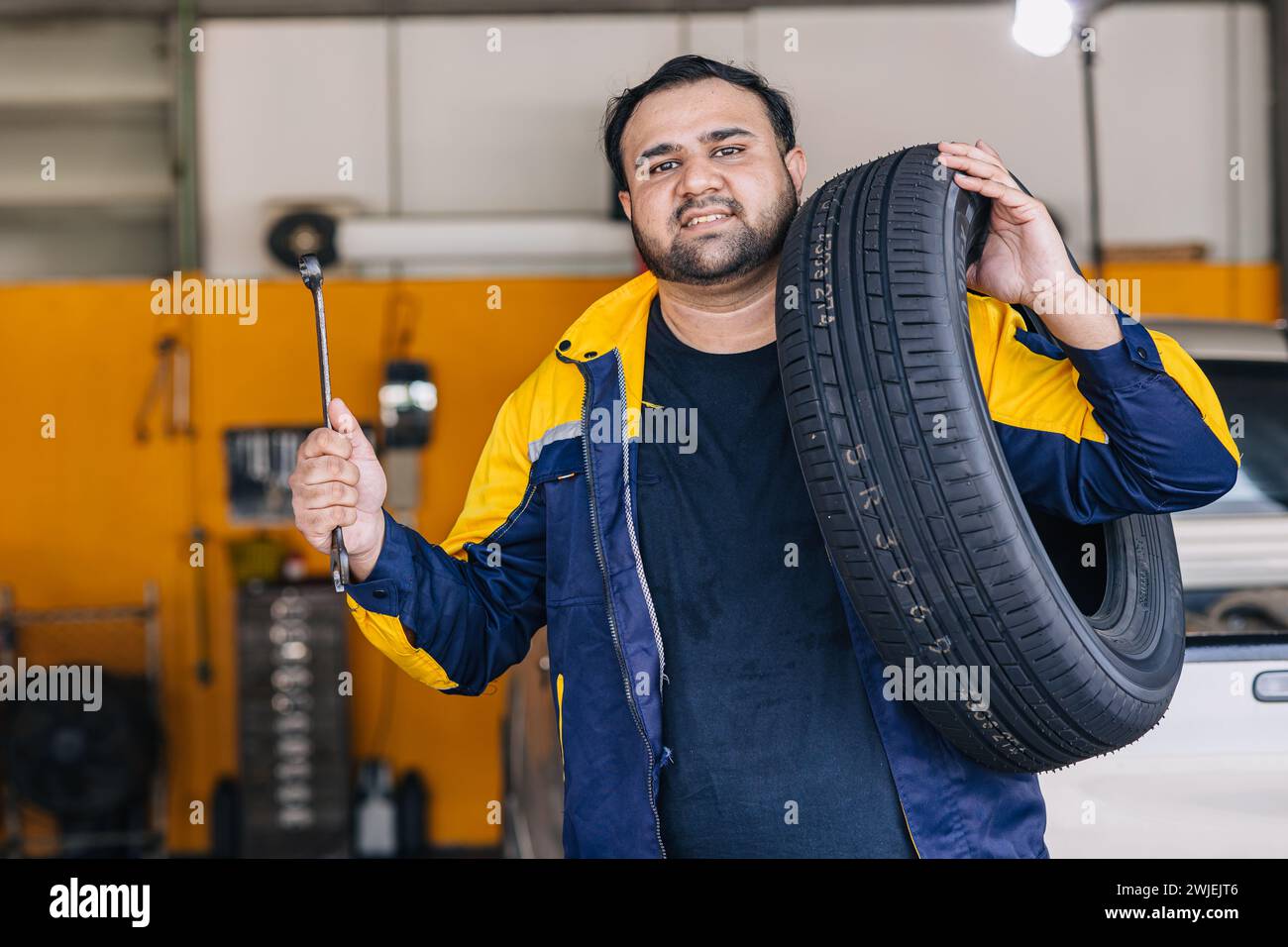 Ritratto indiano uomo lavoratore in garage auto meccanico felice lavoro servizio auto sostituire manutenzione veicolo pneumatico Foto Stock