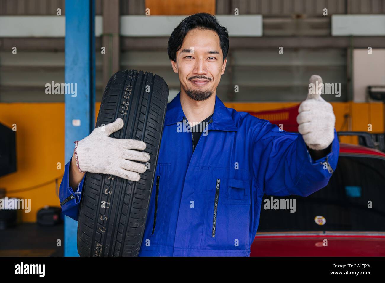 Asiatico giapponese maschio meccanico lavoratore ritratto in auto servizio officina auto pneumatico centro di manutenzione sostituire riparare parte auto Foto Stock