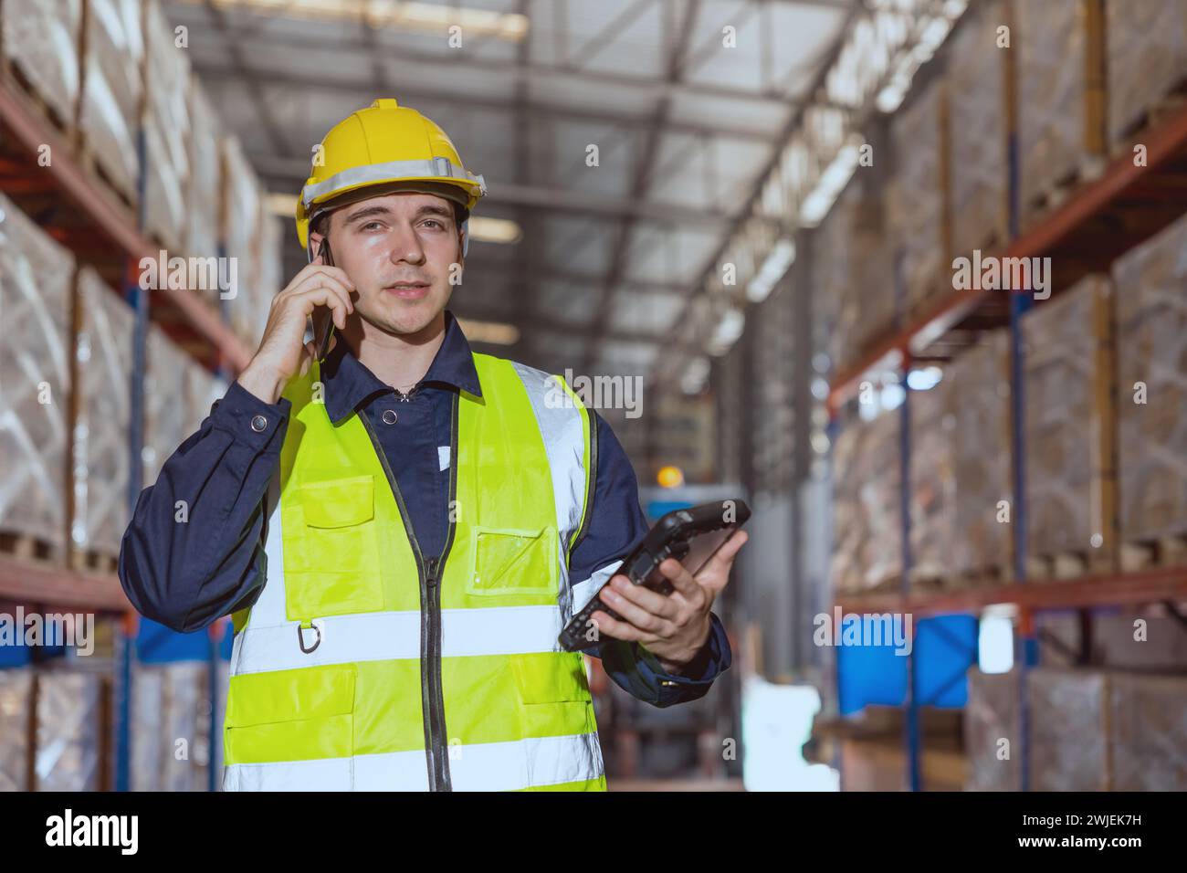 Il magazziniere che utilizza il telefono dello smartphone chiama le persone che si trovano nell'area di stoccaggio del carico della fabbrica. Foto Stock