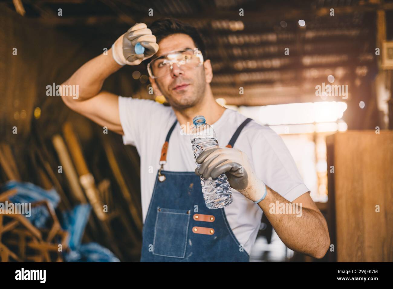 Stress stanco falegname lavoratore sudorazione lavoro duro lavoro di bere acqua freni rilassarsi disidratare in officina di mobili in legno. Foto Stock