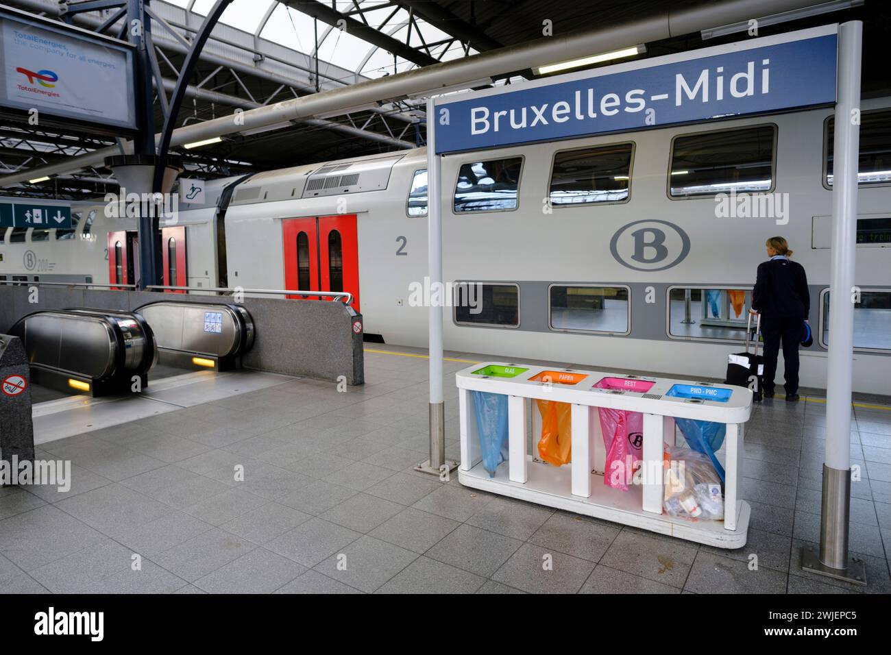 Belgio, Bruxelles: Stazione ferroviaria Bruxelles-Sud. Recipiente per la raccolta differenziata dei rifiuti sotto un cartello Foto Stock