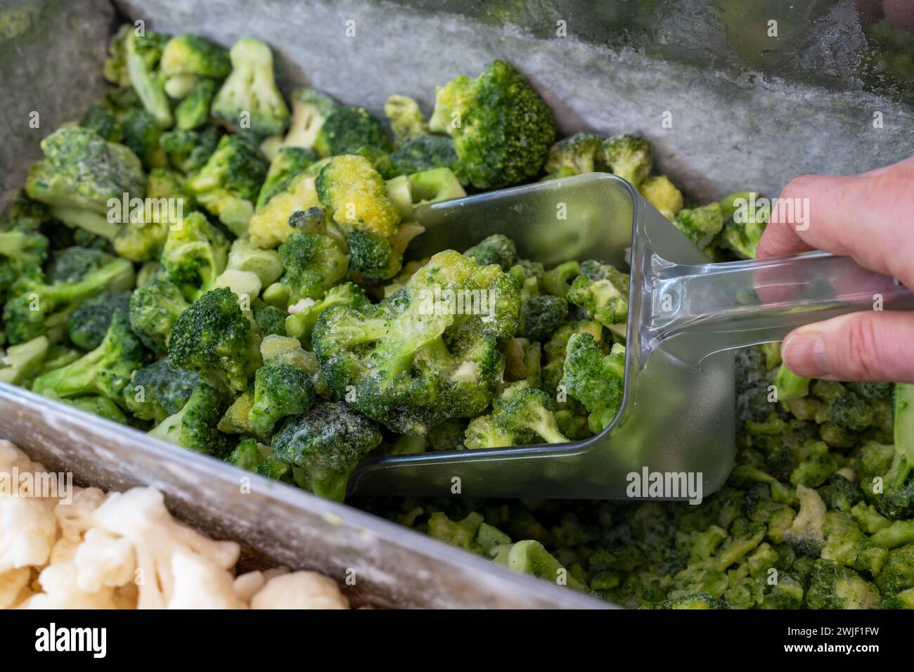 Verdure surgelate. Vendita di broccoli surgelati nel frigorifero di un negozio di alimentari. La mano di un acquirente raccoglie verdure surgelate al supermercato. Foto Stock