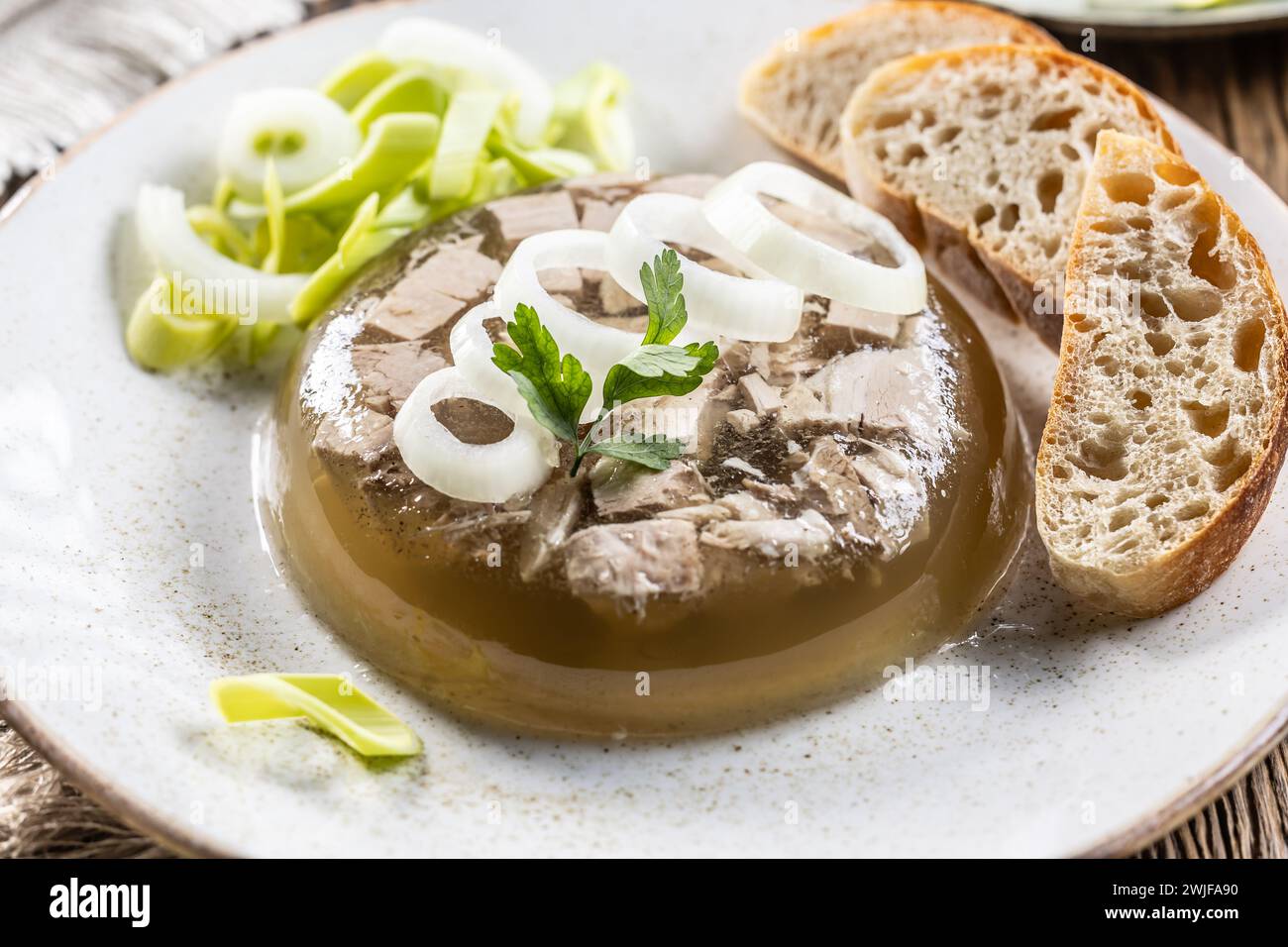 Aspic di maiale fatto in casa, gelatina di carne con cipolla e porro in un piatto bianco. Foto Stock