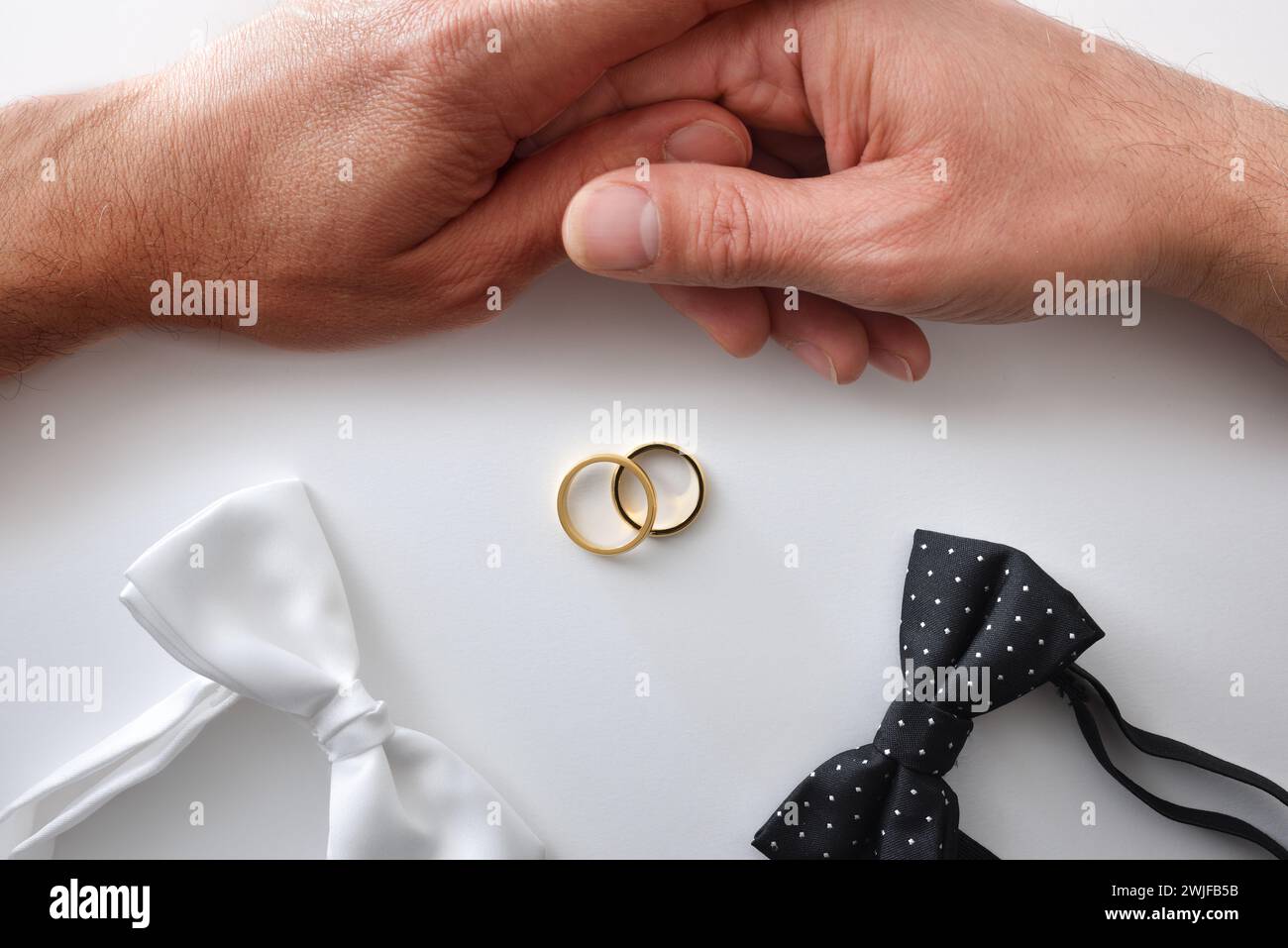 Sfondo concettuale per matrimoni gay con papillon bianco e nero, fedi nuziali al centro e coppia che si tiene per mano. Vista dall'alto. Foto Stock