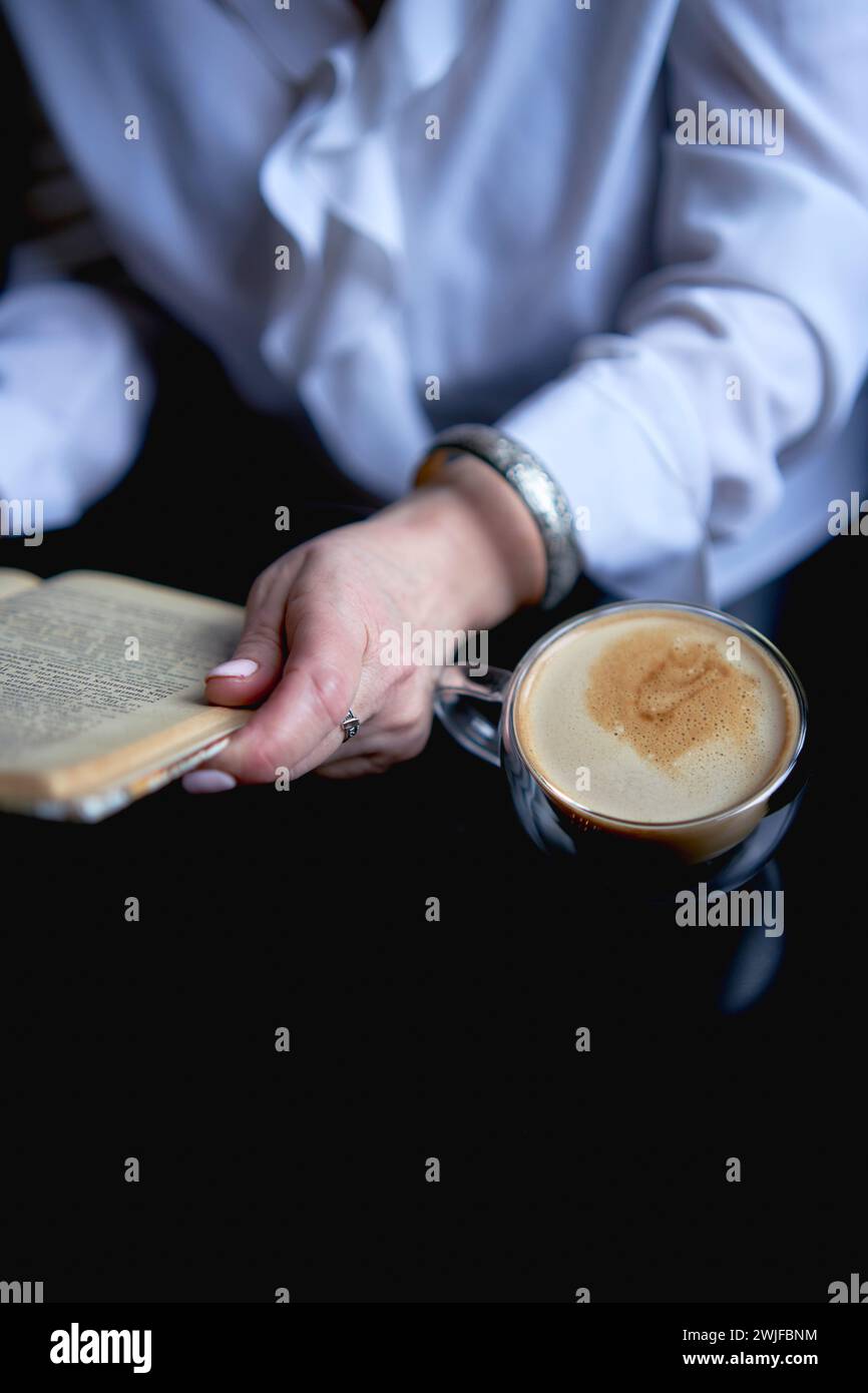 una donna anziana legge un libro in un bar e beve un caffè Foto Stock