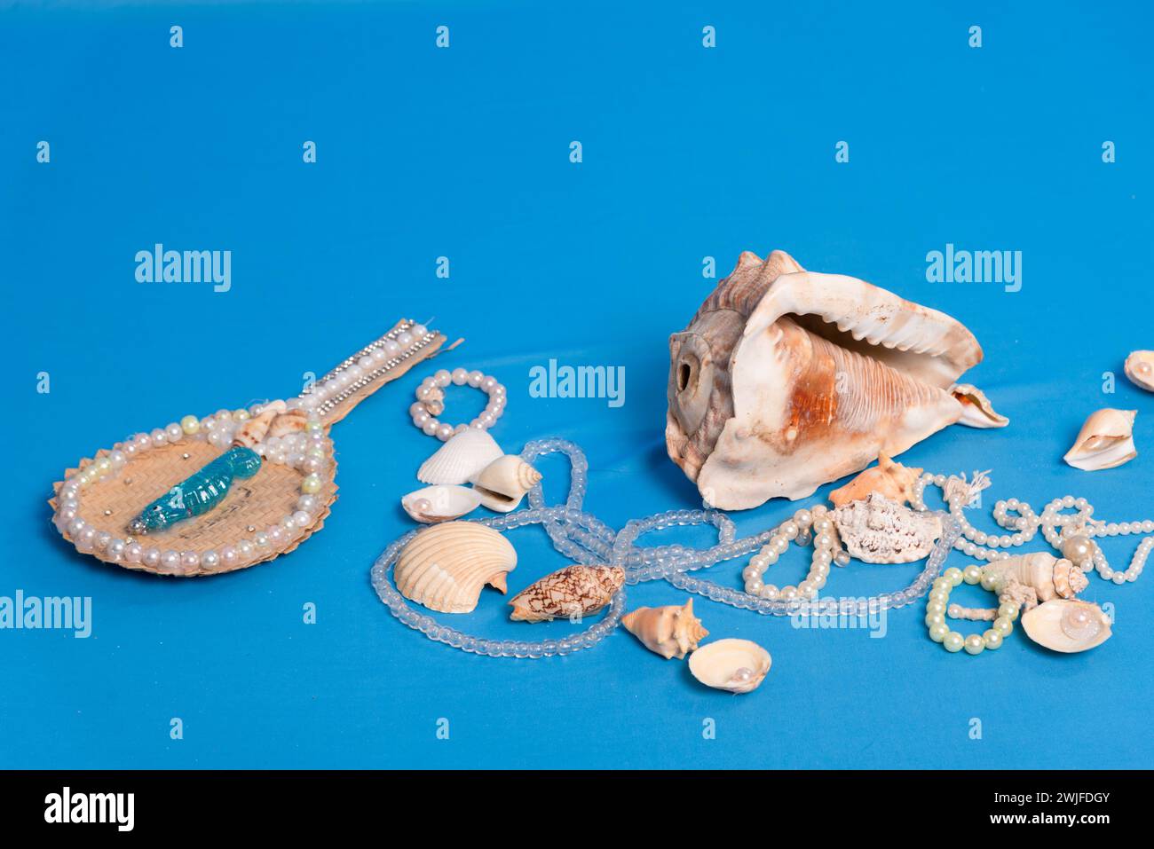 Diverse conchiglie marine, collane e specchi sparsi sul piano blu dello studio. Omaggio a iemanja. Foto Stock
