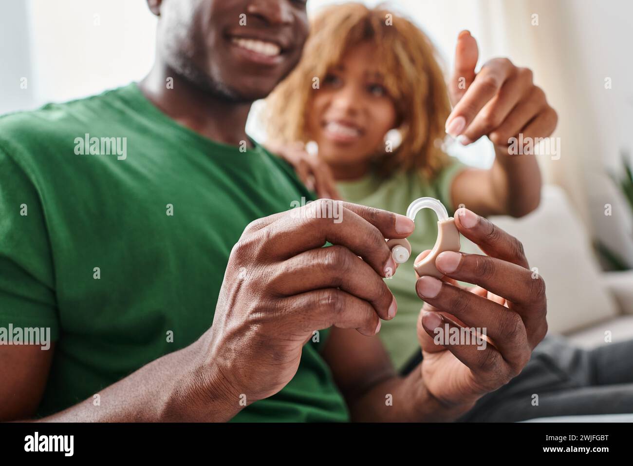 concentrati sull'apparecchio acustico, felice uomo afro-americano che tiene il dispositivo medico vicino alla fidanzata Foto Stock