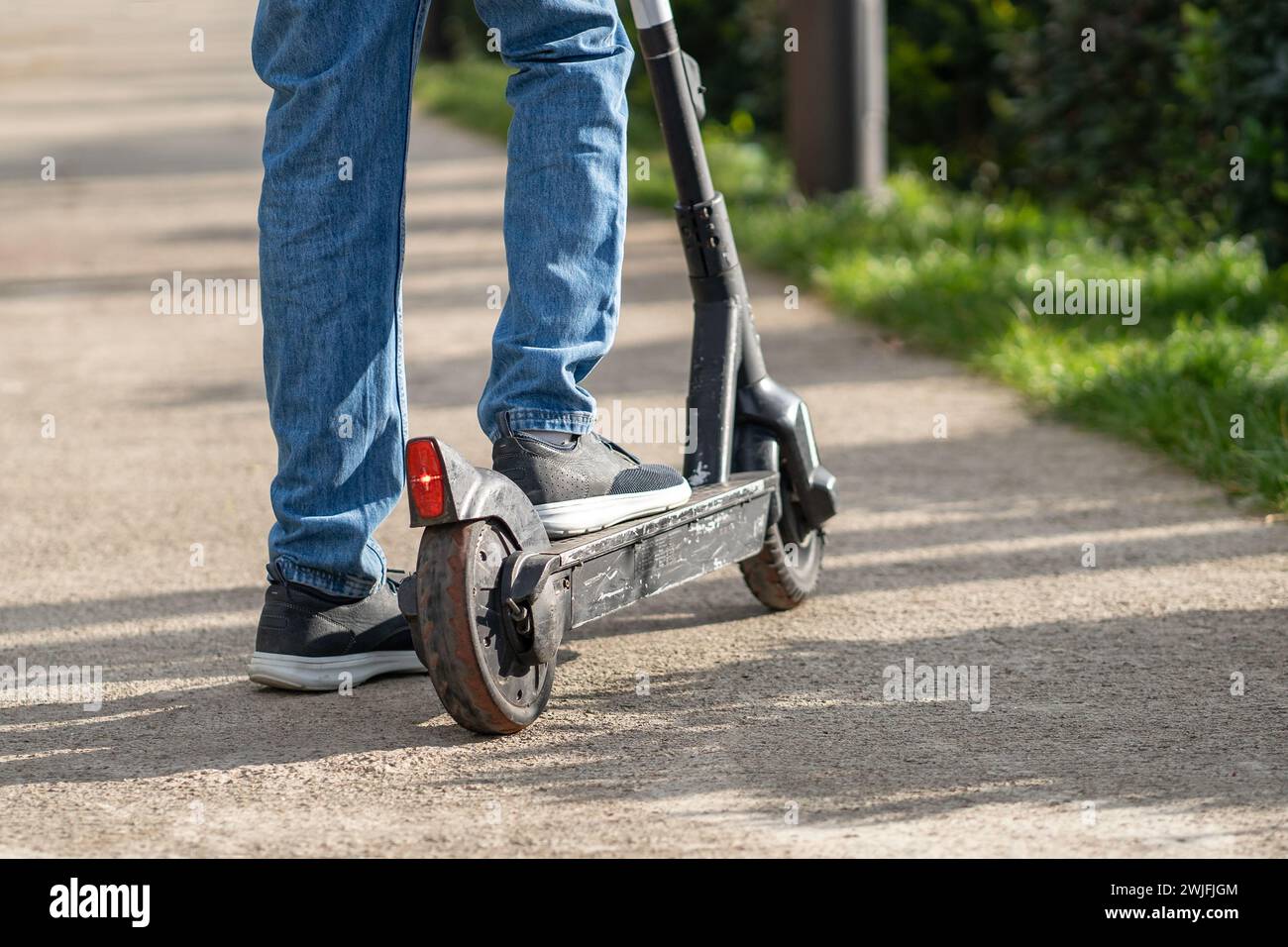 Uomo irriconoscibile alla guida di un vecchio scooter graffiato con pneumatici usurati che richiedono assistenza e riparazione Foto Stock