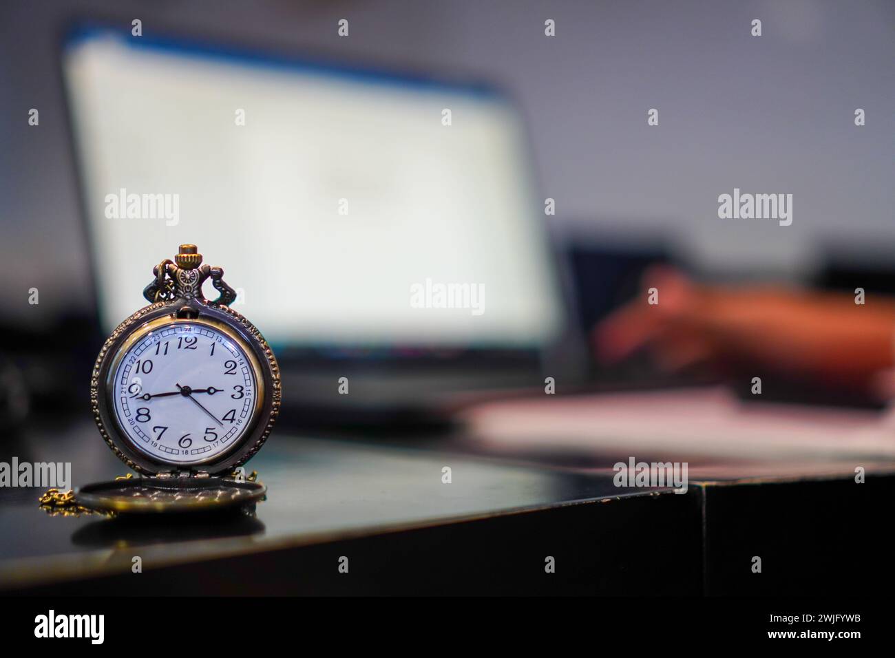 Il tempo e' appena passato. un orologio da tasca classico sullo sfondo di una scrivania affollata con un laptop Foto Stock