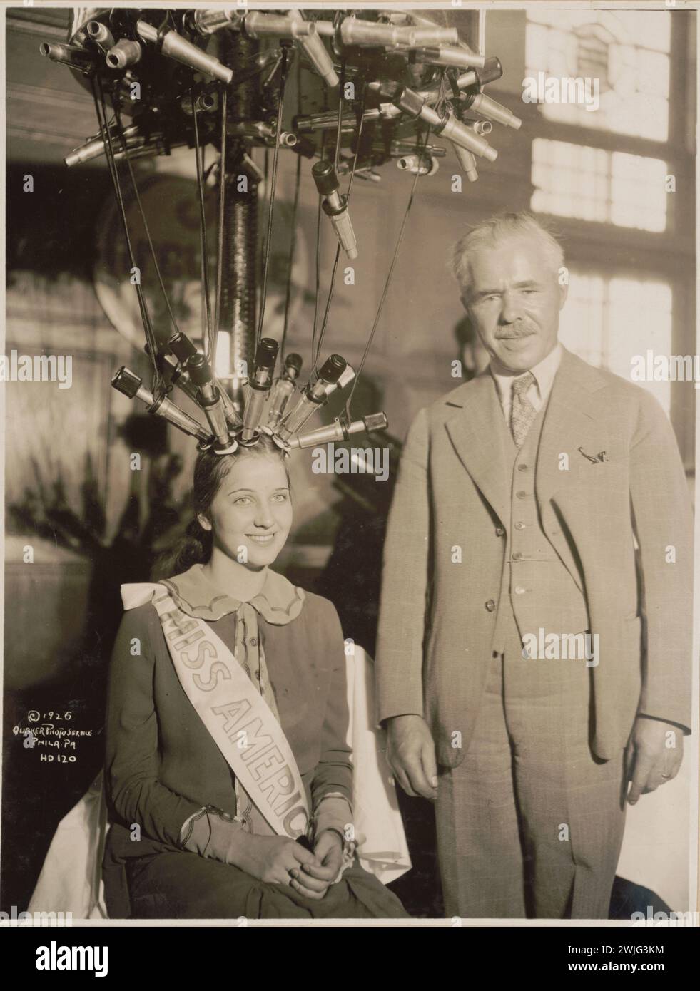 Miss America norma Smallwood, seduta, con i capelli attaccati ad una macchina elettrica a onde permanenti, siede accanto ad un uomo non identificato, Philadelphia, Pennsylvania, 14/10/1926. (Foto di Quaker Photo Service) Foto Stock