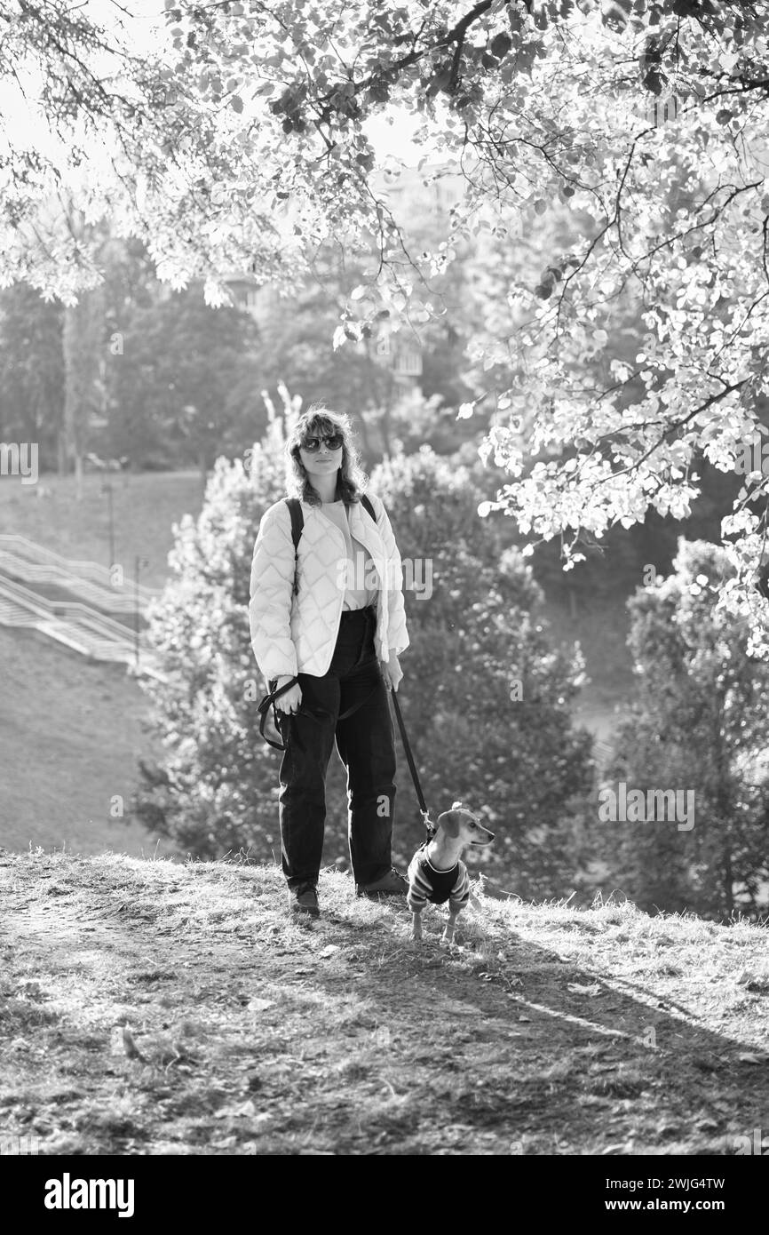 Proprietario che cammina insieme con il cane in un parco all'aperto, vacanze estive, adorabile concetto di animali domestici, amicizia tra l'uomo e il suo animale domestico. Dachshund in maglione foto di alta qualità Foto Stock