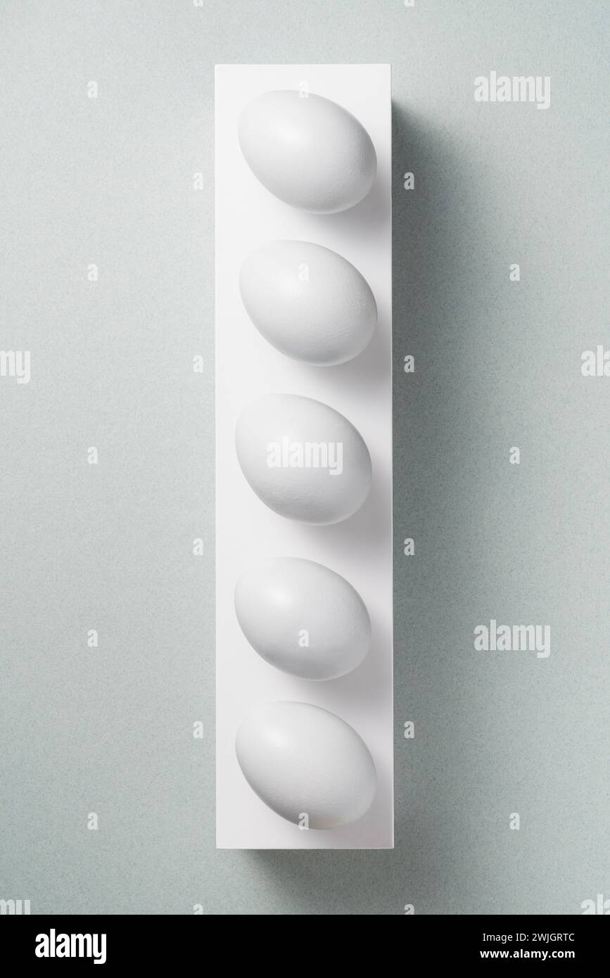 Uova di fila su piedistallo bianco su sfondo grigio Foto Stock