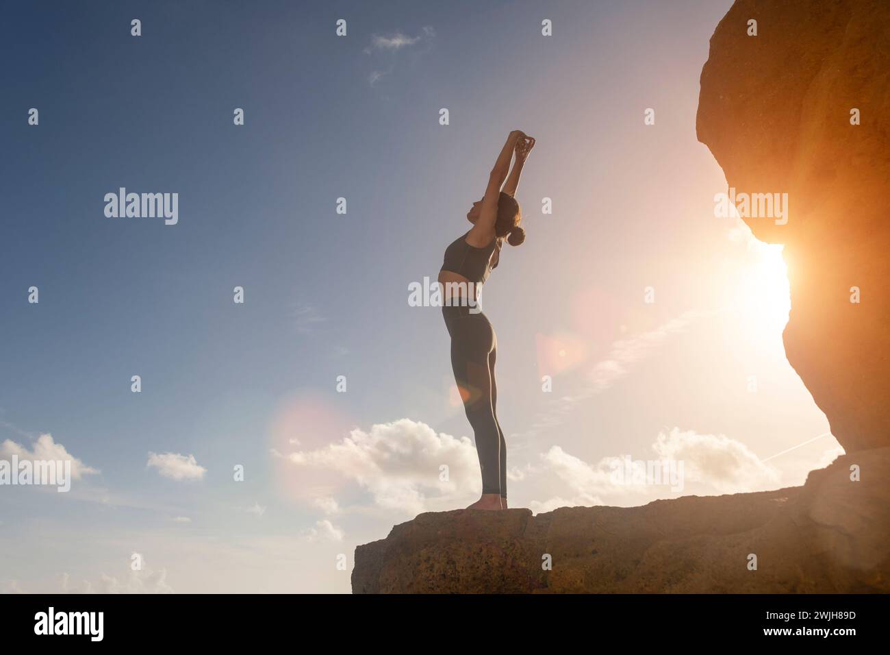 Donna in piedi sulle rocce vicino al mare facendo un backbend, yoga posa. Foto Stock
