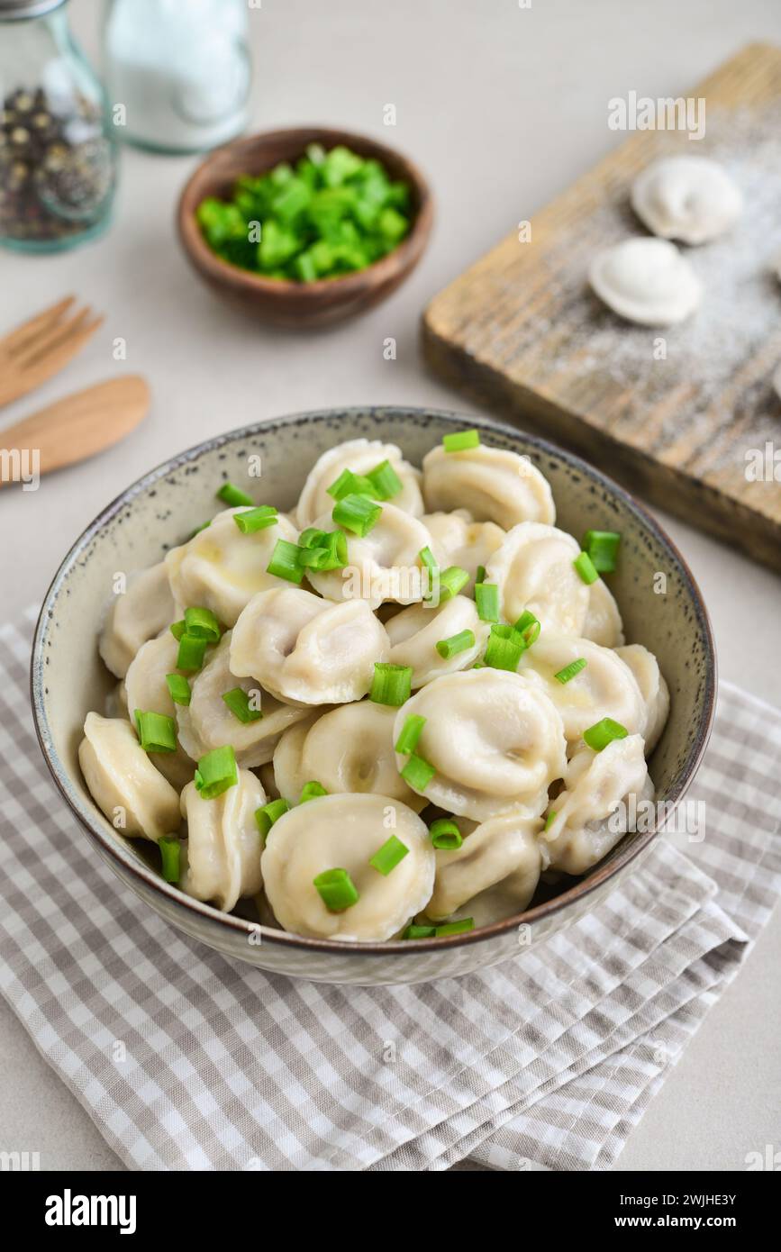 Pelmeni russi, gnocchi con carne, burro ed erbe aromatiche su uno sfondo chiaro Foto Stock