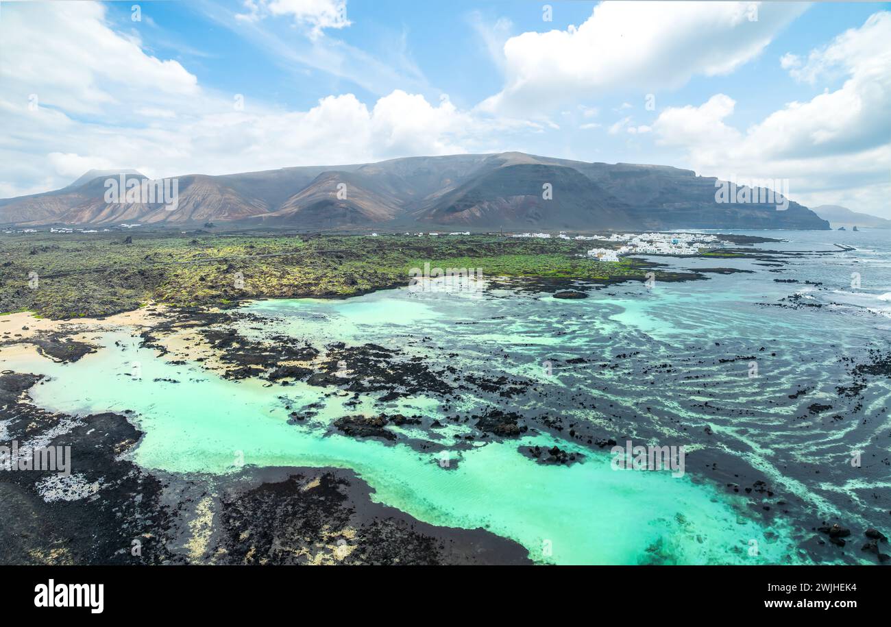 Scopri la tranquilla Caletón Blanco a Lanzarote, dove le rocce vulcaniche cullano le acque turchesi sullo sfondo di spettacolari montagne. Foto Stock