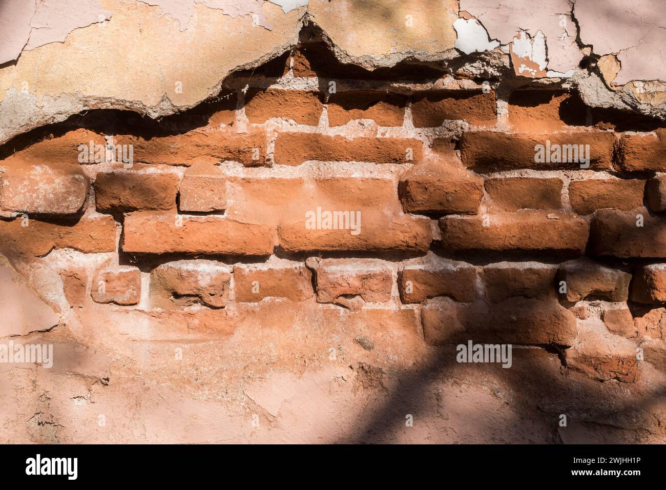 Muro di mattoni con intonaco caduto di una vecchia casa abbandonata in primo piano come sfondo grunge Foto Stock