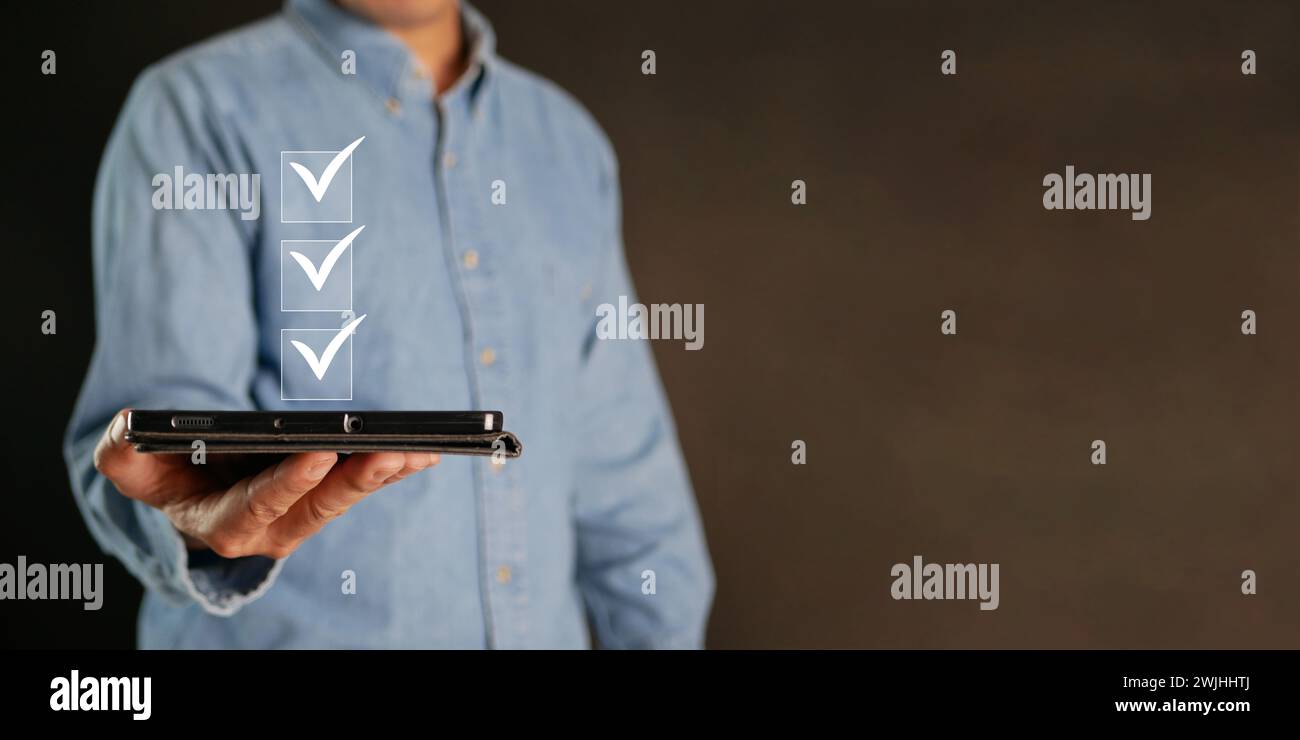 Informazioni sulla lista di controllo. Un uomo con un tablet controlla i segni digitali corretti sulle caselle di controllo. Monitoraggio intelligente delle prestazioni, compilazione del sondaggio online, modulo elettronico Foto Stock