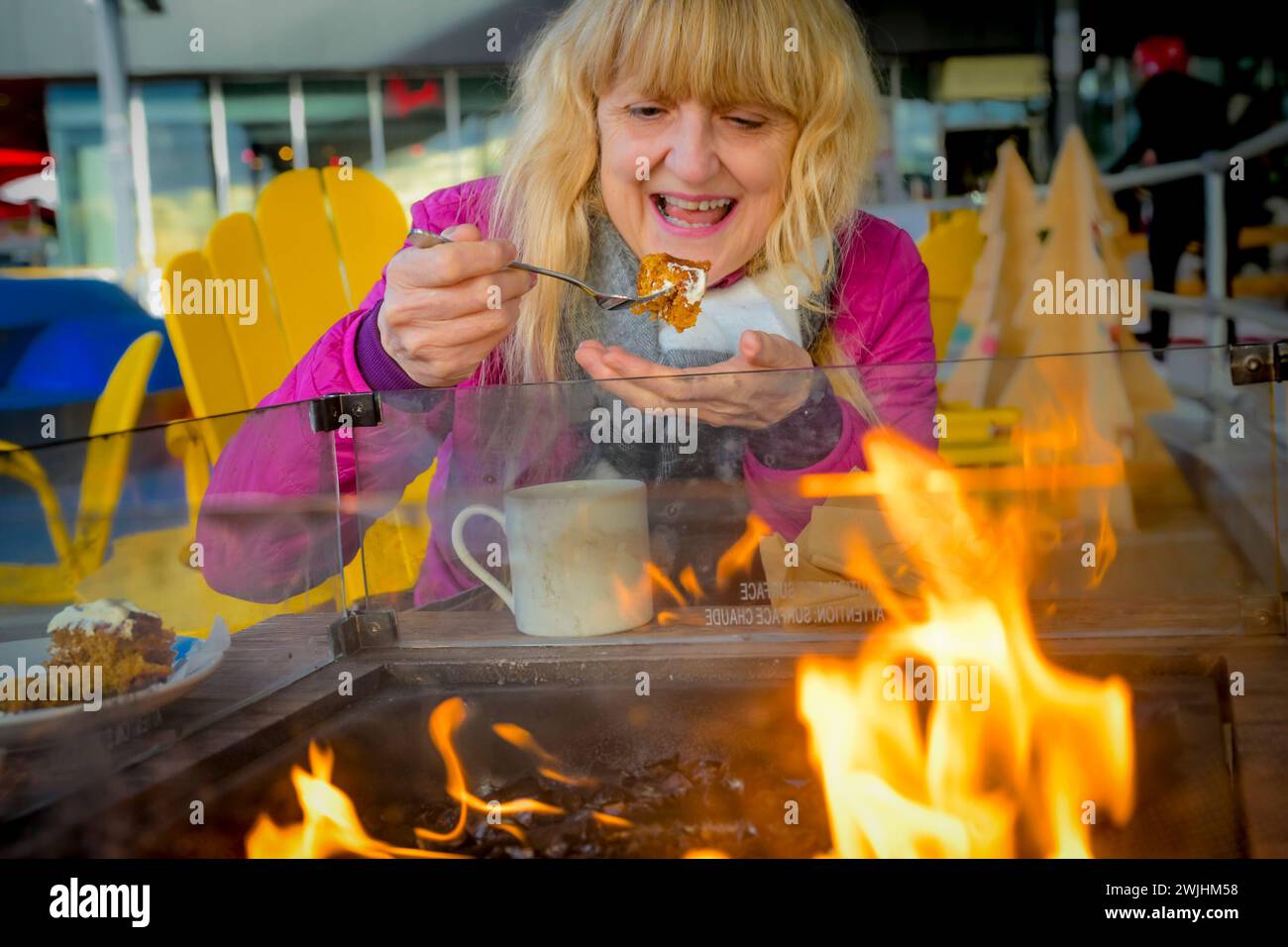 Donna che si gusta un caffè e mangia una torta di carote all'aperto accanto al fuoco caldo in inverno Foto Stock