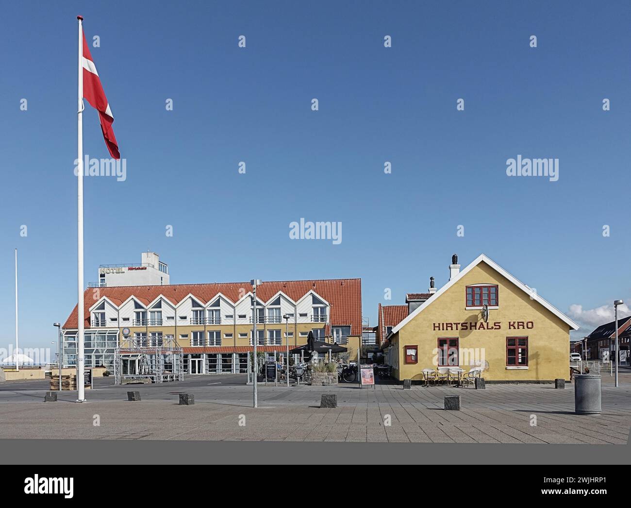 Una bandiera danese vola nel vento di fronte a una fila di edifici moderni sotto un cielo azzurro, Danimarca, Jutland settentrionale, Hitshals Foto Stock
