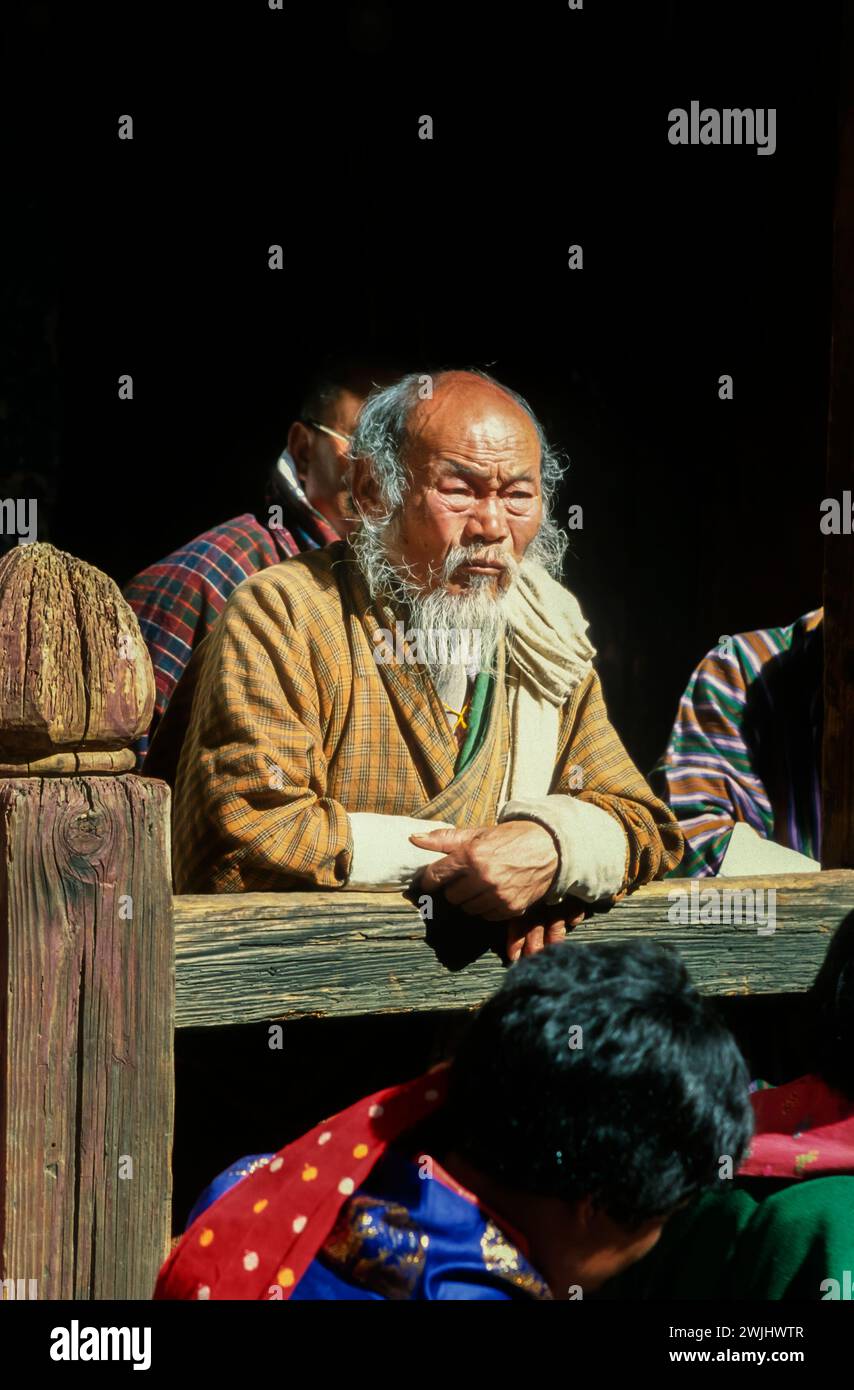 Spettatori locali al Jakar Dzong Tsechu, un popolare festival religioso e culturale annuale celebrato in ottobre a Jakar Dzong nella valle di Bumthang, nel Bhutan centrale. Una varietà di danze colorate con maschere sono condotte da monaci che sono sviluppati secondo precise istruzioni date dai maestri buddisti del passato. Un anziano uomo del posto con una barba sgargiante guarda la performance. Foto Stock