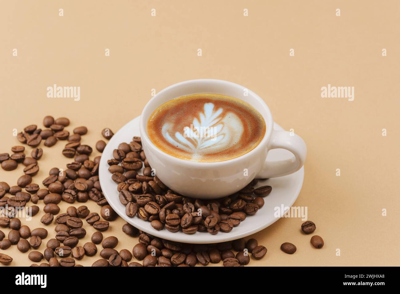 Una tazza di caffè con arte del caffè e chicchi di caffè su sfondo beige. Foto Stock