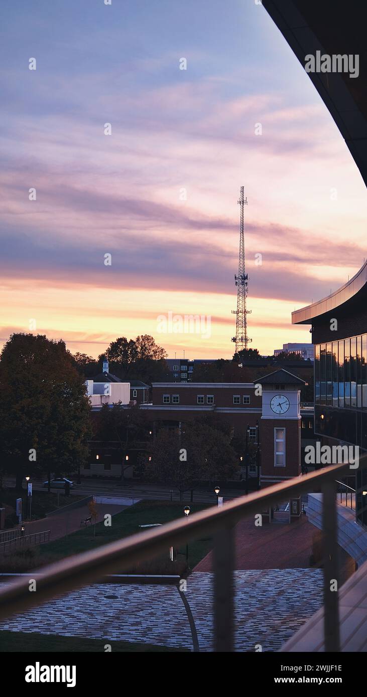 Una vista serale al tramonto del Central Piedmont Community College con edifici universitari, una torre di segnalazione cellulare in lontananza e una torre dell'orologio sul lato della strada. Foto Stock