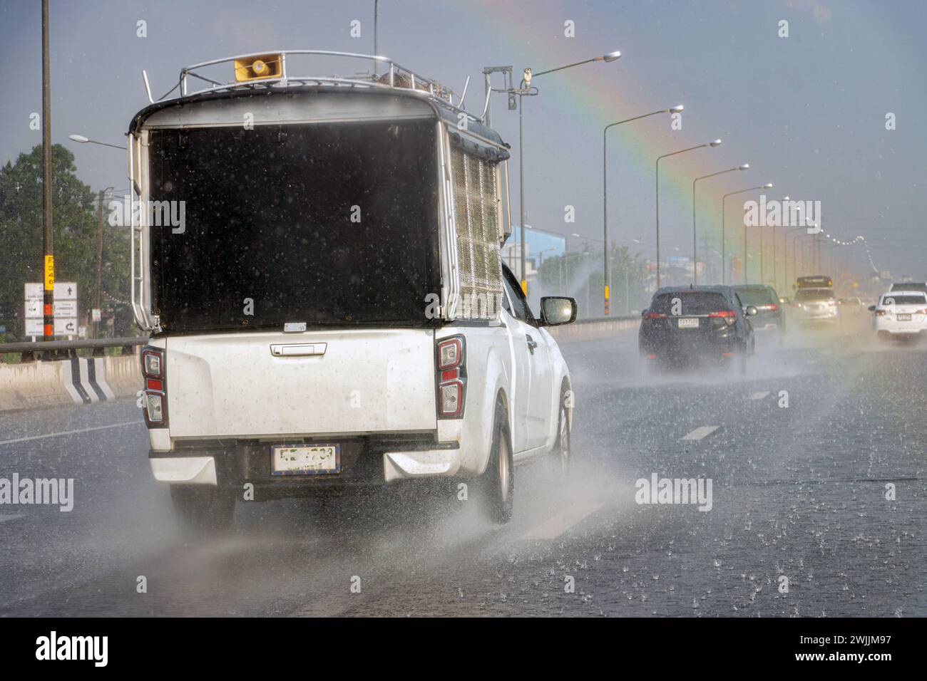 Traffico stradale in forte pioggia con arcobaleno colorato nel cielo Foto Stock