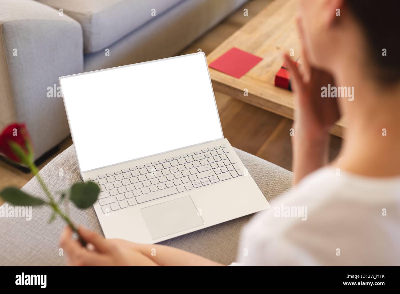 Una giovane donna viene vista da dietro tenendo in mano una rosa mentre guarda lo schermo di un notebook, con spazio per le copie Foto Stock