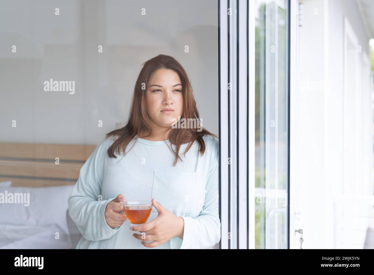 Una giovane donna birazziale di grandi dimensioni gode di un momento di pace a casa, sorseggiando un drink Foto Stock