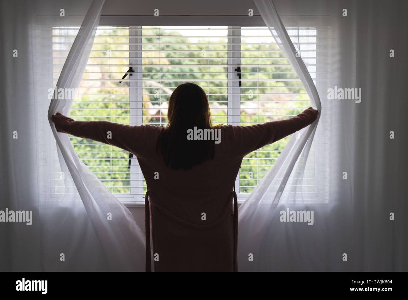 La donna apre le tende per accogliere la luce del mattino a casa Foto Stock