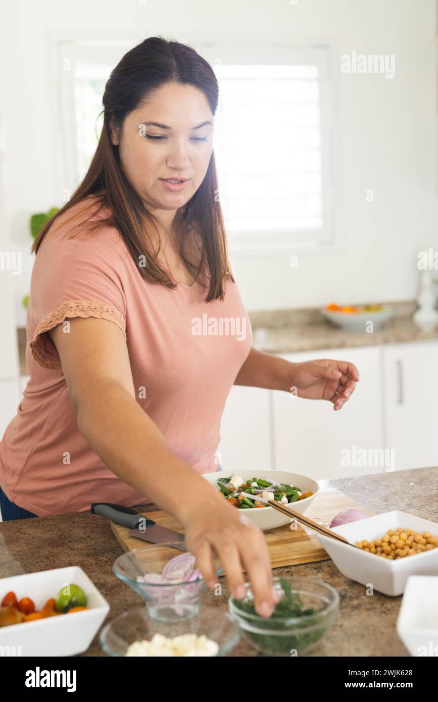 Una giovane donna birazziale di grandi dimensioni prepara un'insalata in una cucina di casa Foto Stock