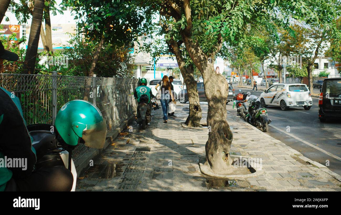 Sotto i cieli soleggiati della città di Medan, un operaio Gojek naviga lungo la strada pedonale, incarnando la mobilità urbana e la vitalità Foto Stock