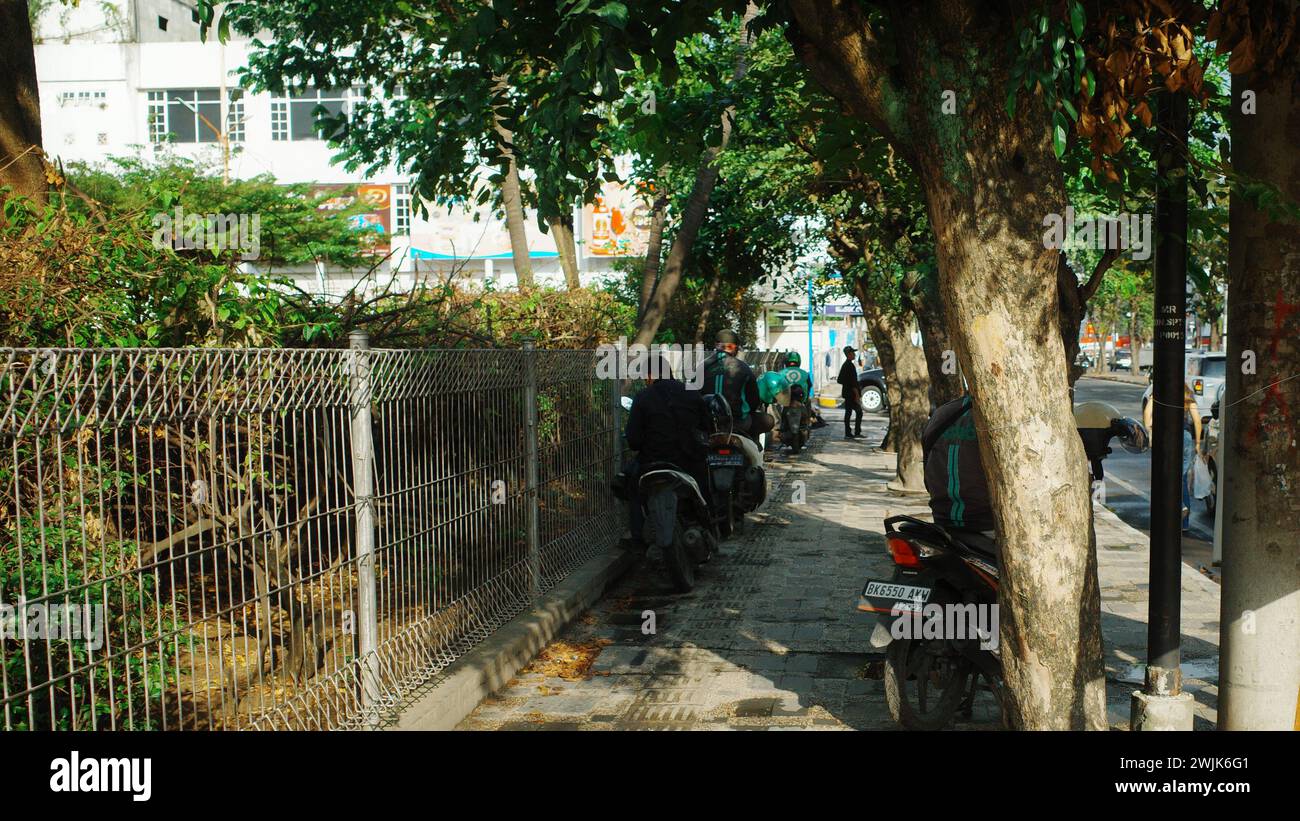 Sotto i cieli soleggiati della città di Medan, un operaio Gojek naviga lungo la strada pedonale, incarnando la mobilità urbana e la vitalità Foto Stock