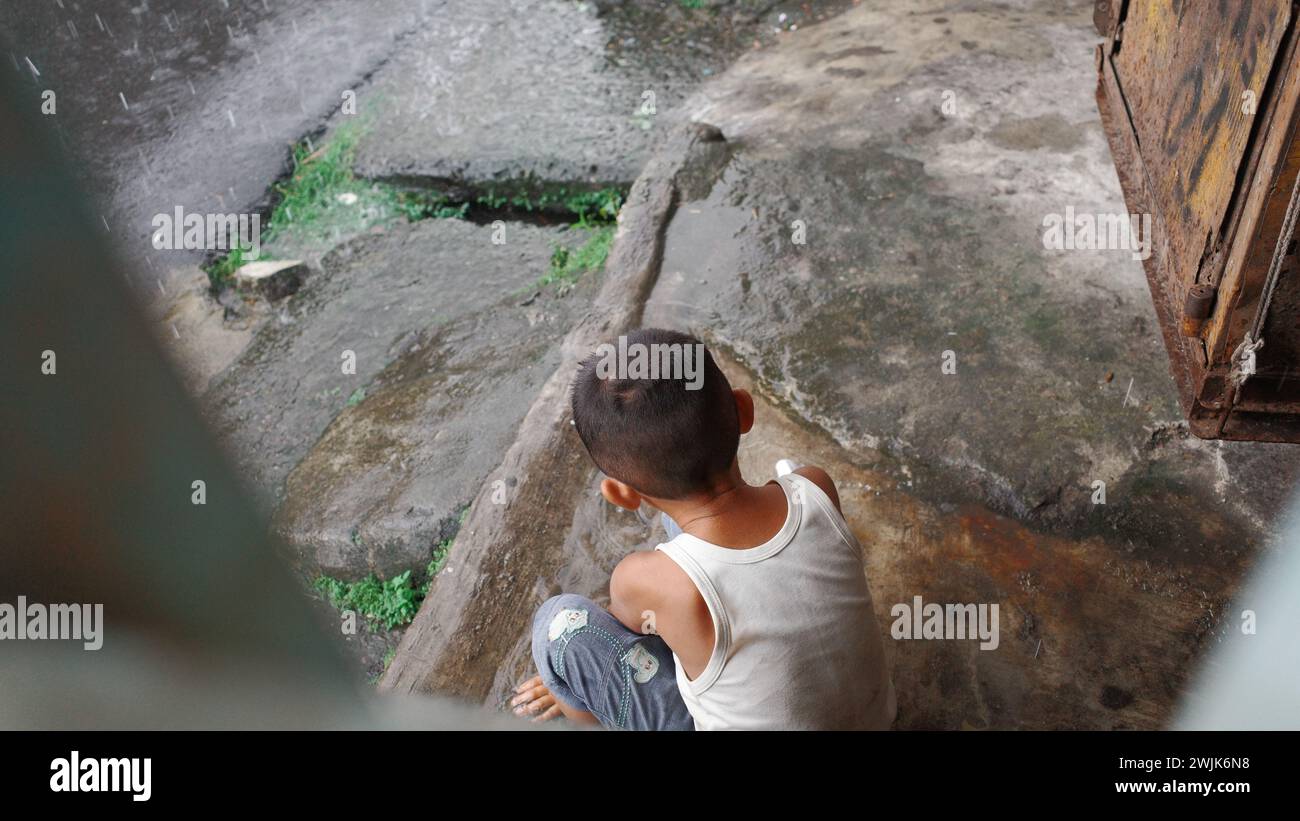 In mezzo al vivace paesaggio urbano di Medan, un bambino trova conforto nella solitudine giocosa ai margini della città, creando avventure di immaginazione Foto Stock