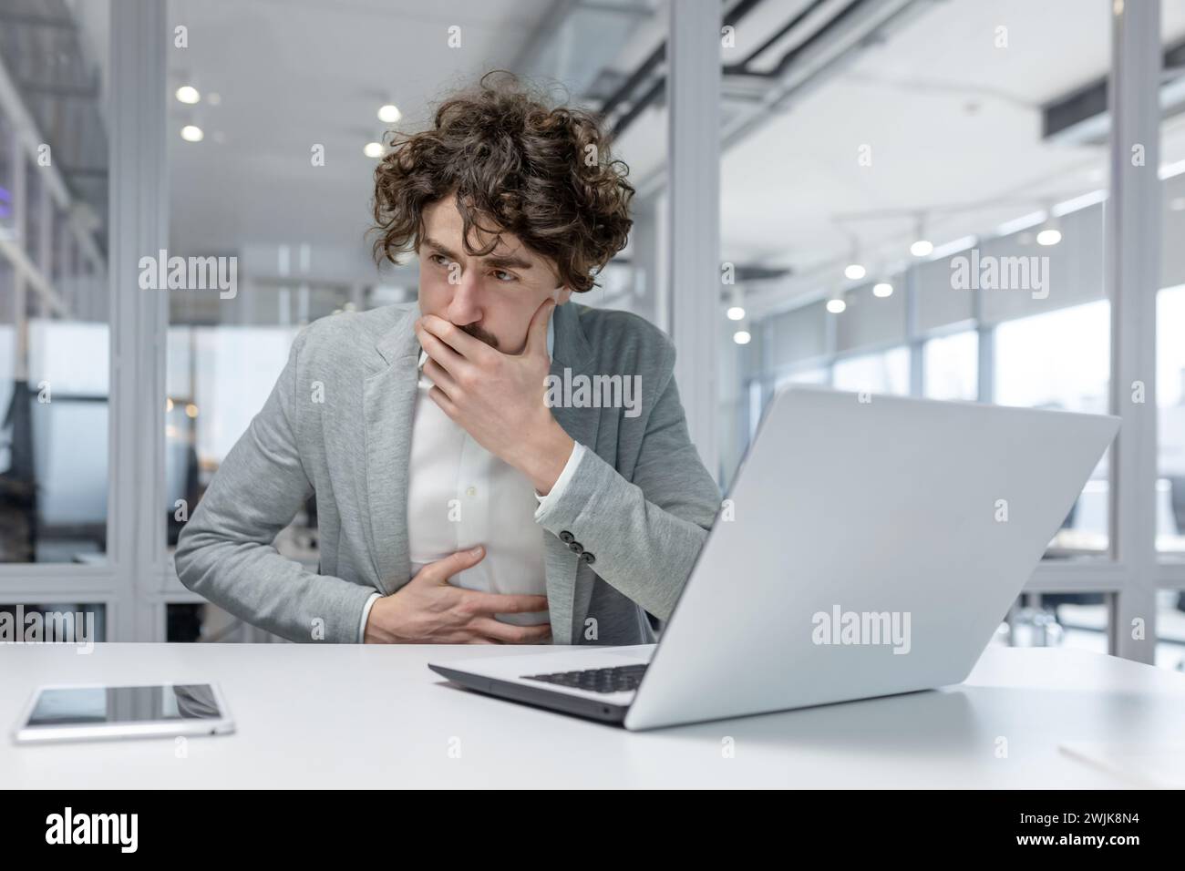 Uomo dai capelli ricci che lavora con attenzione su un notebook in ufficio, trasudando esperienza e concentrazione. Foto Stock