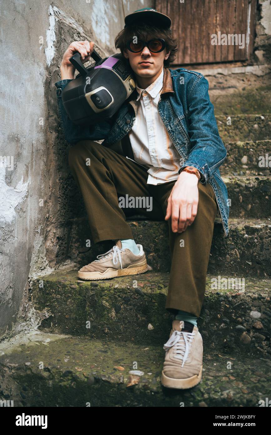 Uomo che tiene il boombox sulla spalla seduto sulle scale. concetto di nostalgia in stile retrò anni '90. Foto Stock