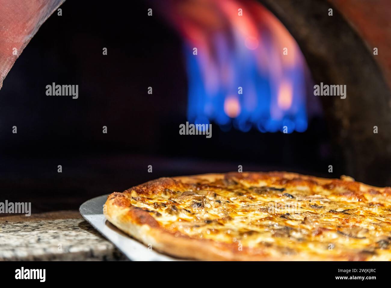 Pizza mista fresca dal forno con fiamme visibili sullo sfondo Foto Stock