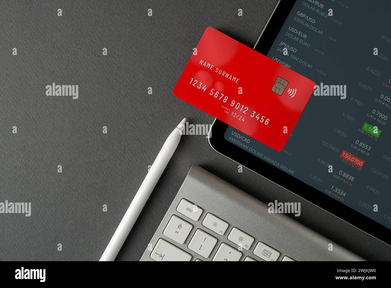 Vista dall'alto del tablet con tassi di cambio in tempo reale sullo schermo, carta di credito rossa e tastiera su tabella nera Foto Stock
