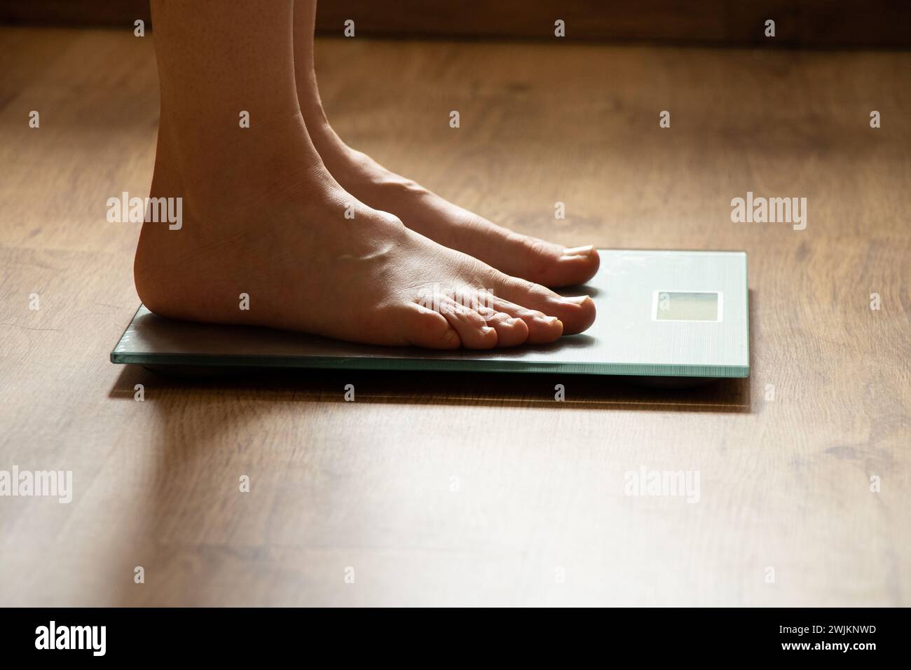 I piedi della donna sono appoggiati sulla bilancia del bagno a casa sul pavimento, sotto la luce Foto Stock